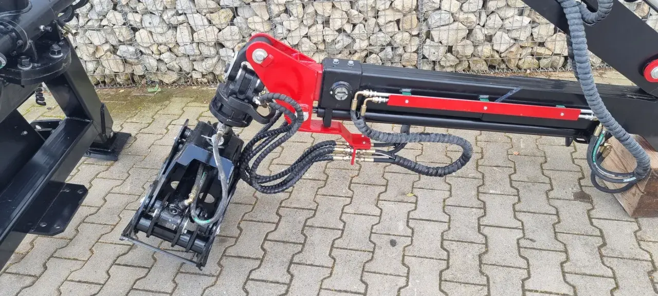 Detailaufnahme eines roten und schwarzen Schwenkwerks für Forstkran mit Greifer und Hydraulikschläuchen.