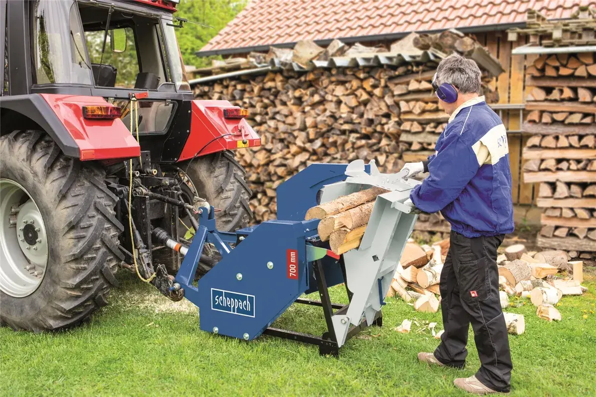Mann bedient eine gebrauchte Scheppach Rolltischkreissäge mit Zapfwellenantrieb, bereit zum Holzhacken neben einem Traktor.