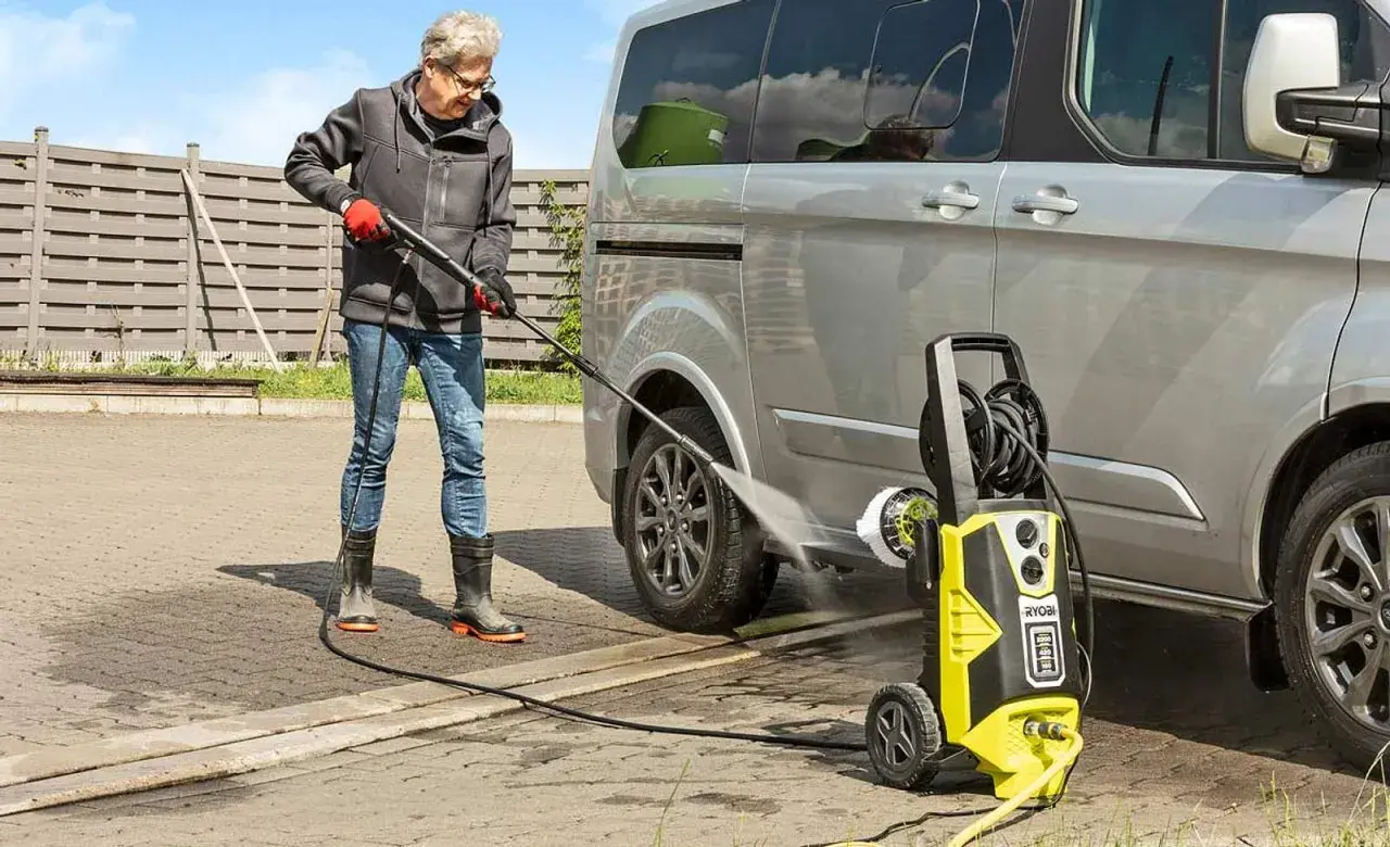 Mann reinigt Auto mit **Hochdruckreiniger**. Der **Kompressor**-ähnliche Reiniger sprüht kräftig Wasser.