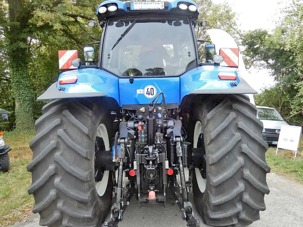 Blauer Traktor mit gro&szlig;en Reifen. An den Seiten sind rot-wei&szlig;e Parkwarntafeln angebracht.