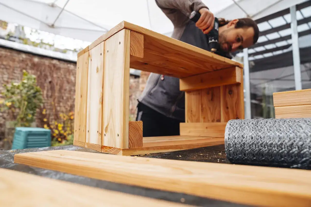 Mann schraubt an einem Holzkasten, der als Wurmbox selber bauen Projekt dient. Draußen, unter einem Vordach, entstehen neue Projekte.