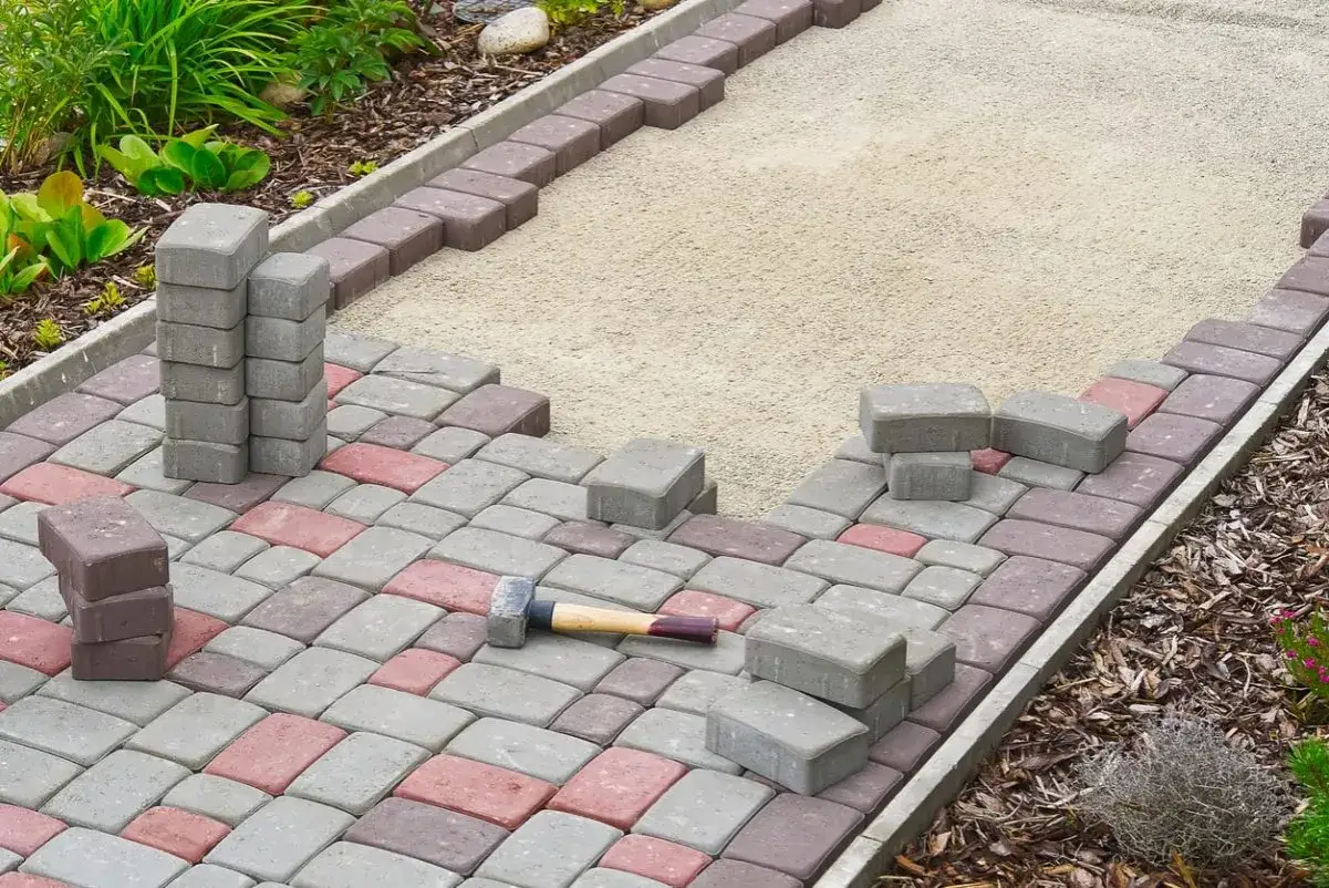 Gartenweg wird mit roten und grauen Steinen verlegt. Ein Gummihammer liegt bereit.