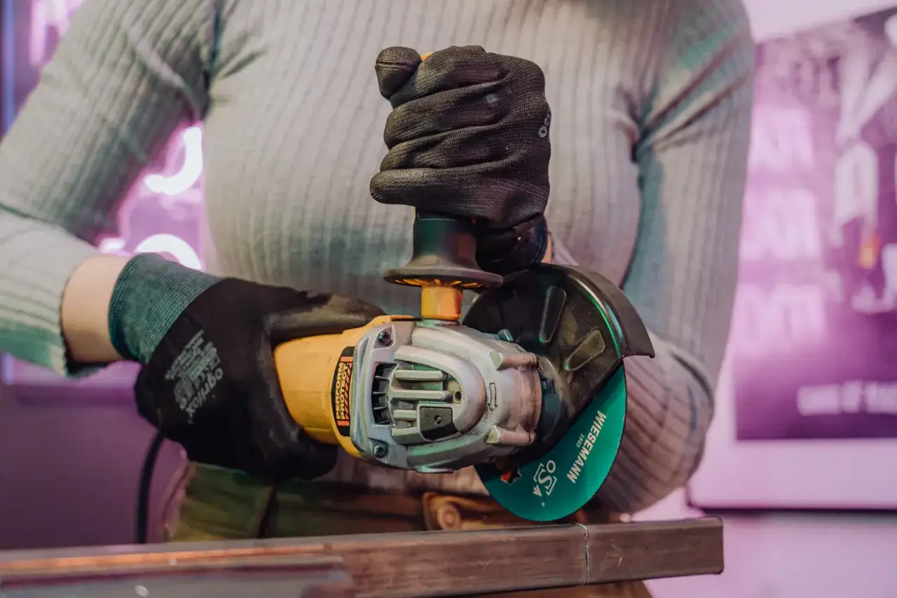 Person mit Handschuhen bereitet sich darauf vor, mit einem Winkelschleifer Metall zu flexen.