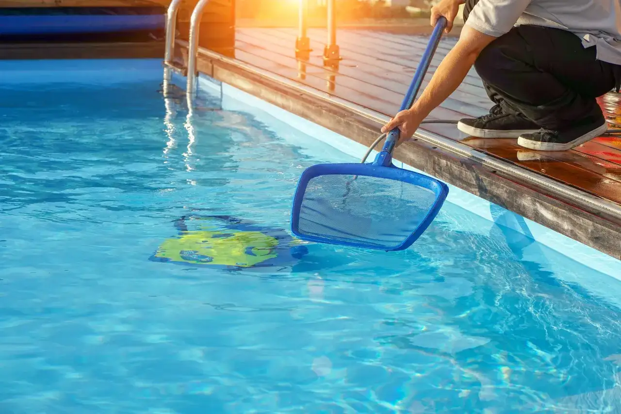 Mann reinigt einen Frame Pool mit einem Kescher. Ein gelber Schwimmring treibt im klaren Wasser.
