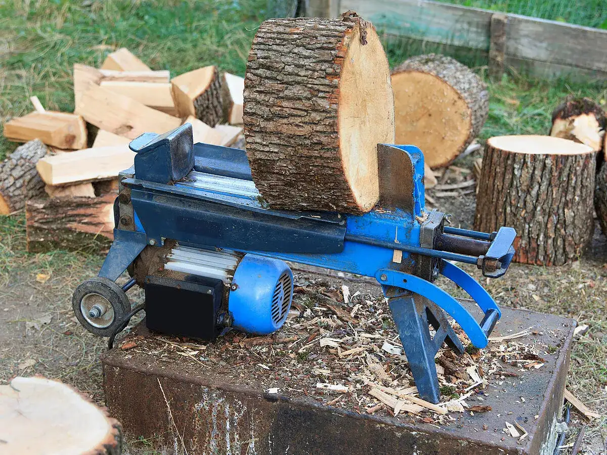 Blauer cmi holzspalter 6t mit einem Holzstamm bereit zum Spalten, umgeben von Holzscheiten und Baumstümpfen.