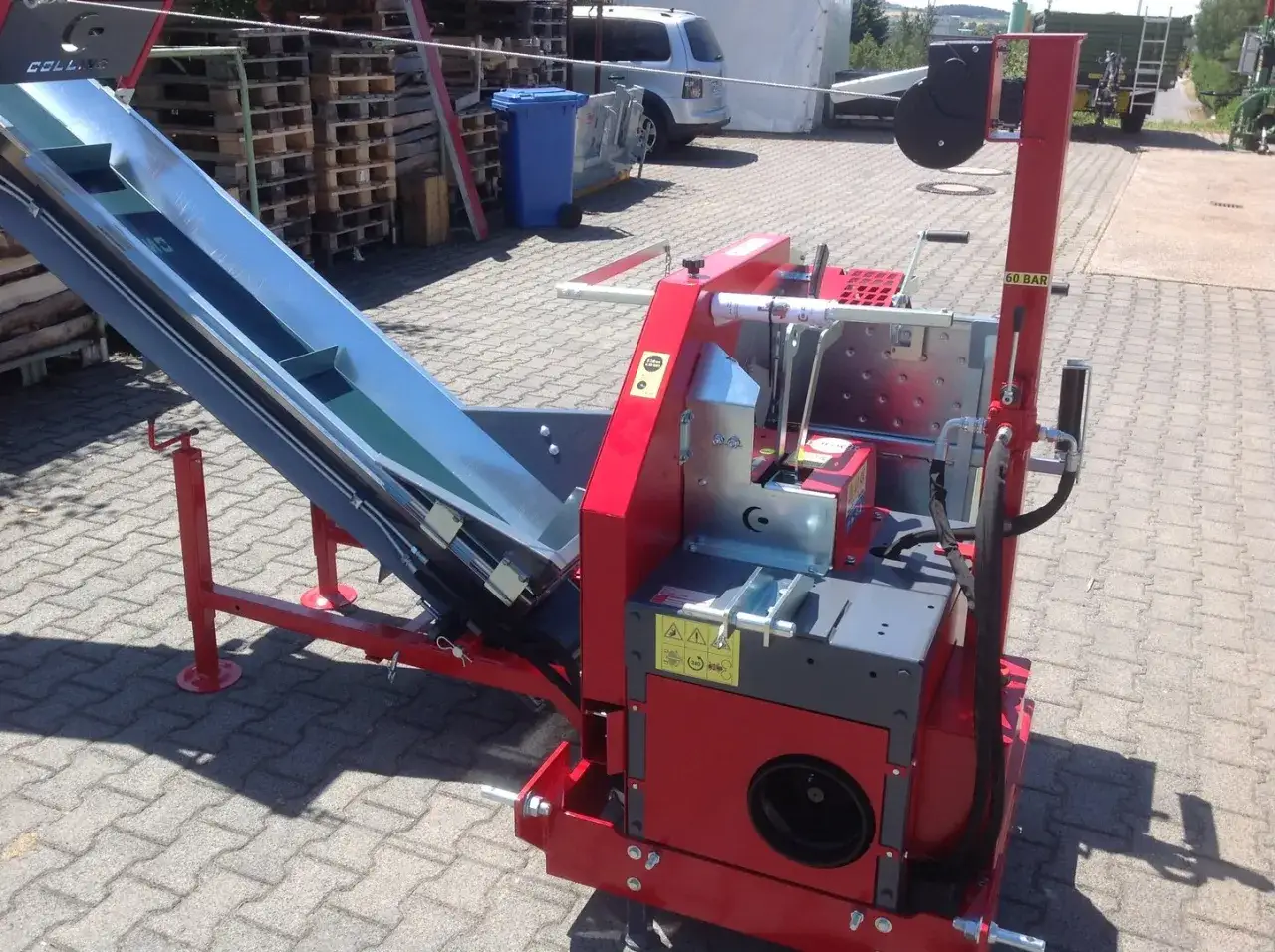 Rote Maschine mit einem langen, schrägen Förderband, bereit für den Einsatz. Diese Kreissäge mit Förderband ist ein robustes Gerät für die Holzverarbeitung.
