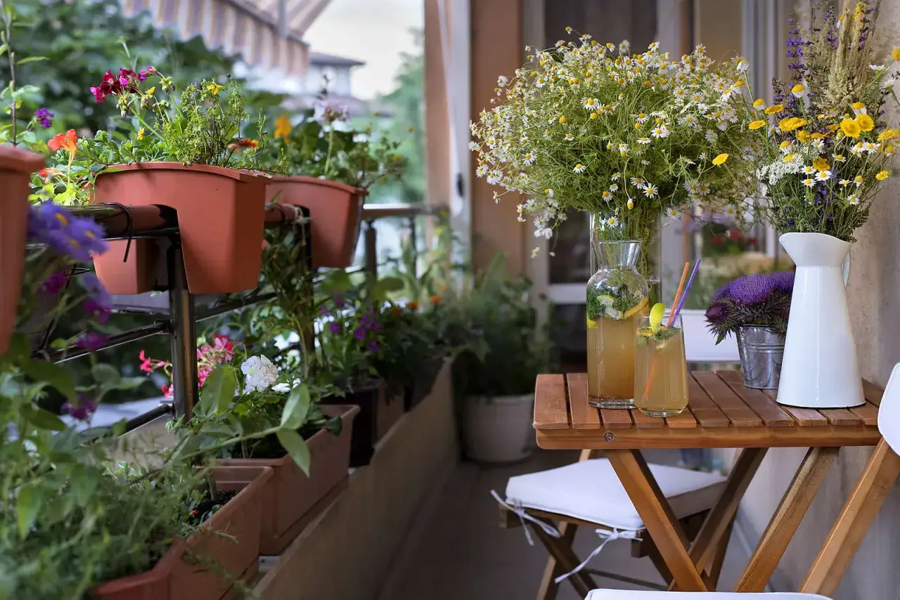 Blumenkästen mit bunten Blumen und Kräutern, die beste Balkonpflanzen für ein sommerliches Ambiente. Ein Tisch mit erfrischenden Getränken und Blumenarrangements.