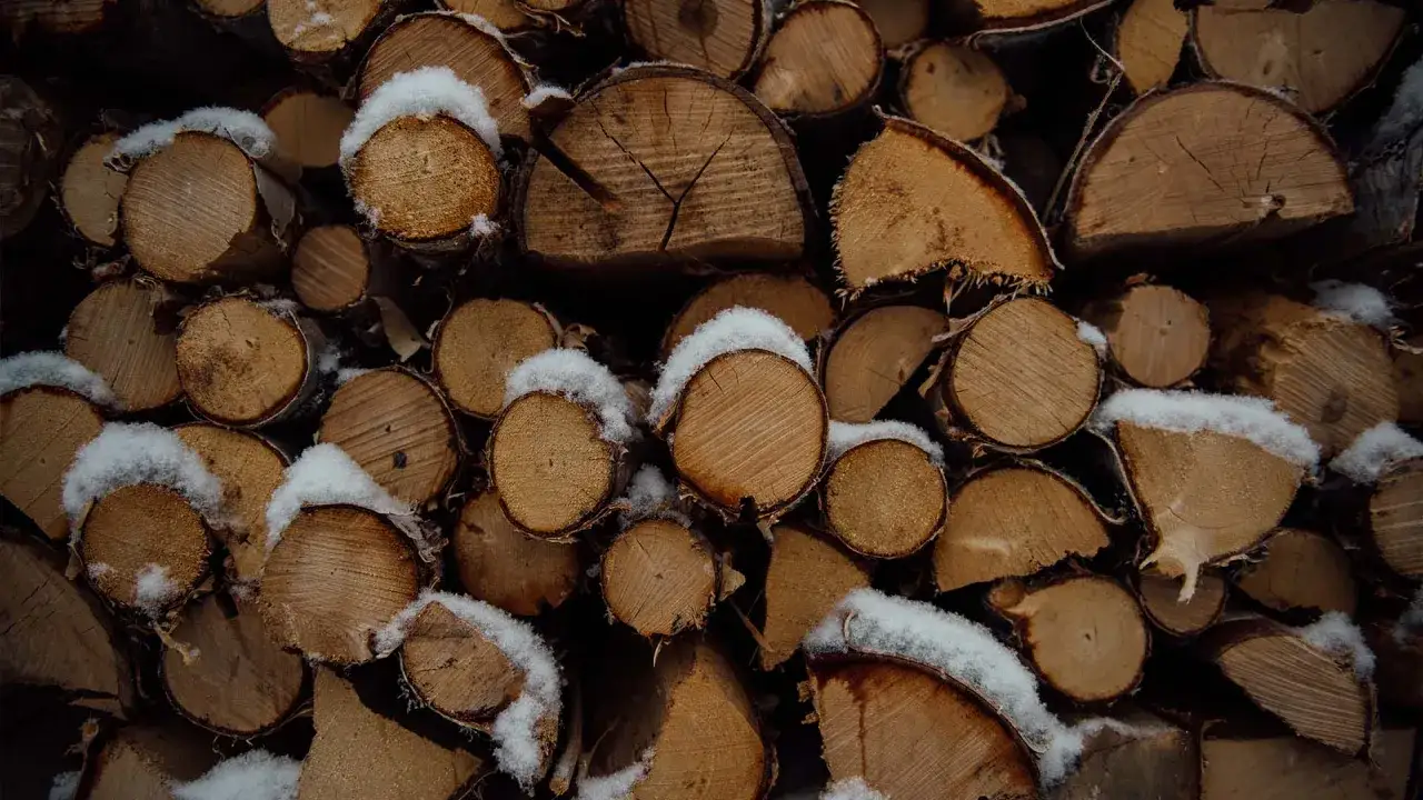 Stapel von gespaltenem Bauholz, bedeckt mit Schnee, bereit, im Kamin zu verbrennen und Wärme zu spenden.