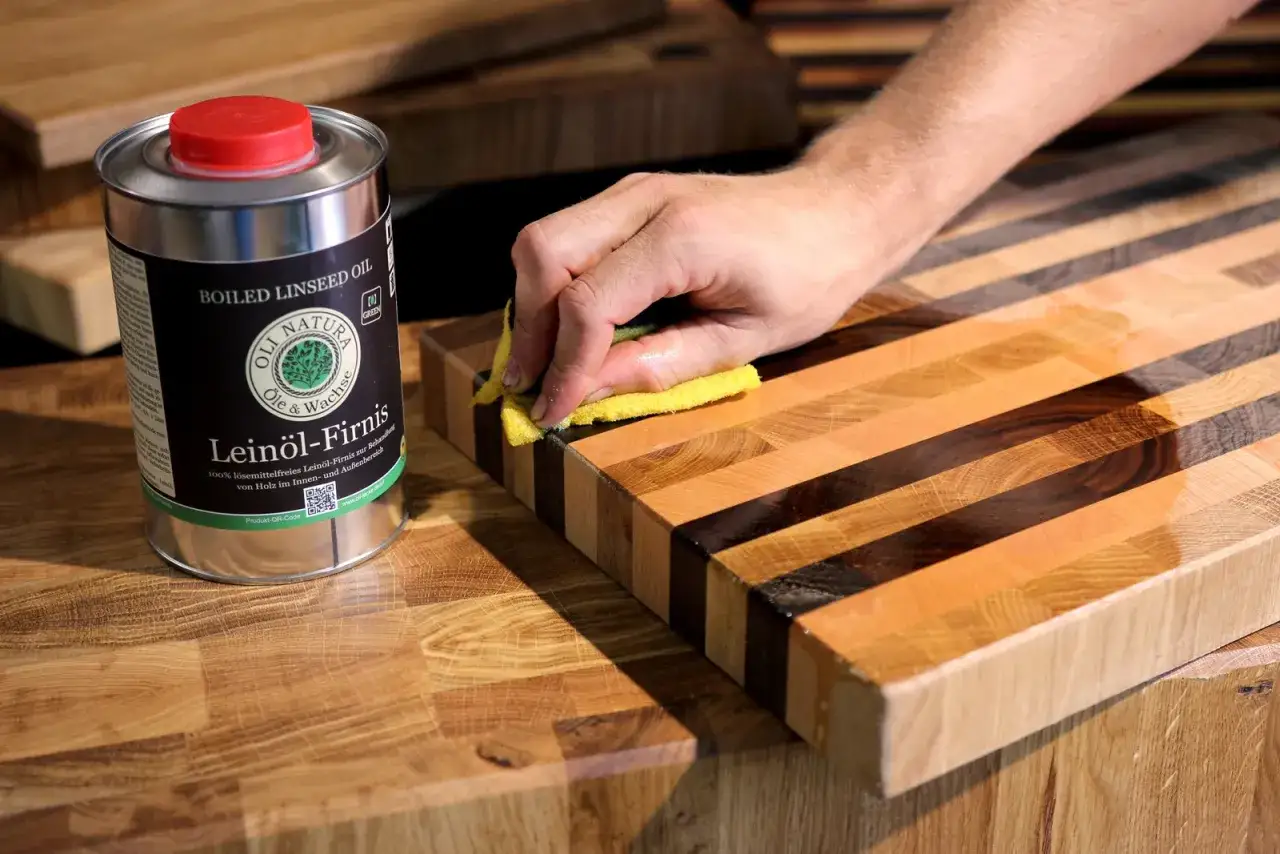 Hand behandelt ein Holzbrett mit Leinöl-Firnis. Die Dose mit dem Öl steht daneben.
