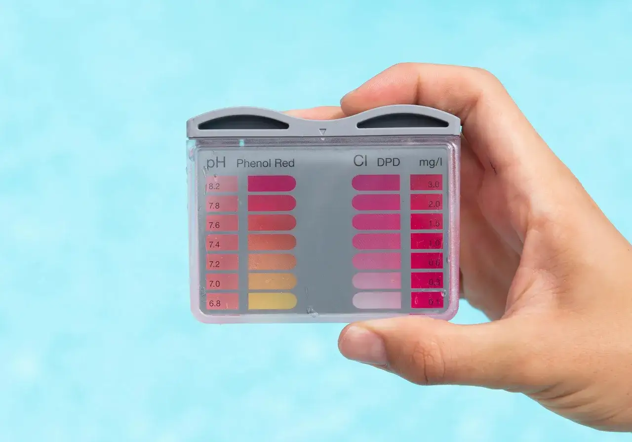 Hand hält Pool-Teststreifen zur Bestimmung des optimalen pH-Werts und Chlorgehalts.