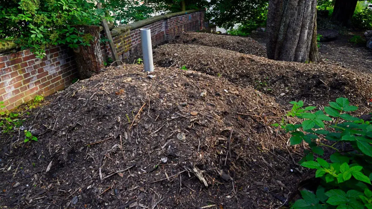 Große Komposthaufen aus Laub und Ästen, bereit für die Verwendung im Garten. Ein Rohr ragt aus dem vorderen Haufen.