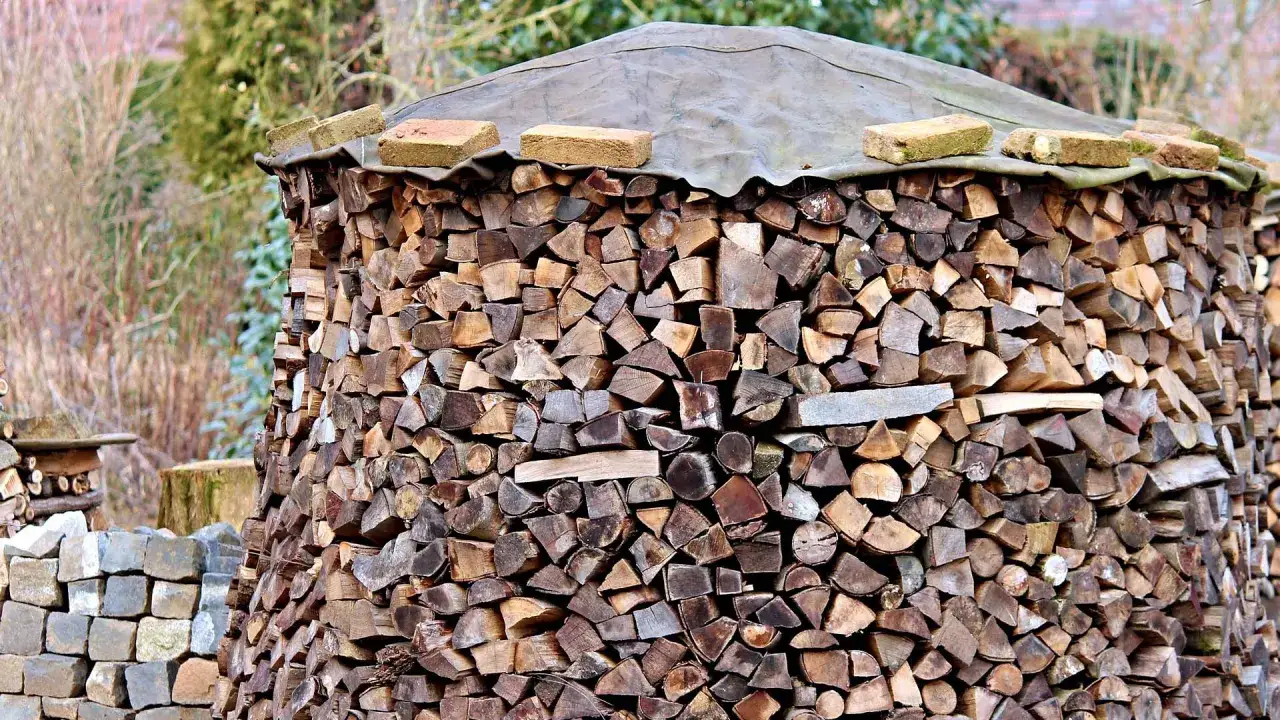 Ein großer Stapel gespaltenes Holz, bereit zum Bongossi Holz verbrennen. Ziegelsteine und eine Plane schützen die oberste Schicht.