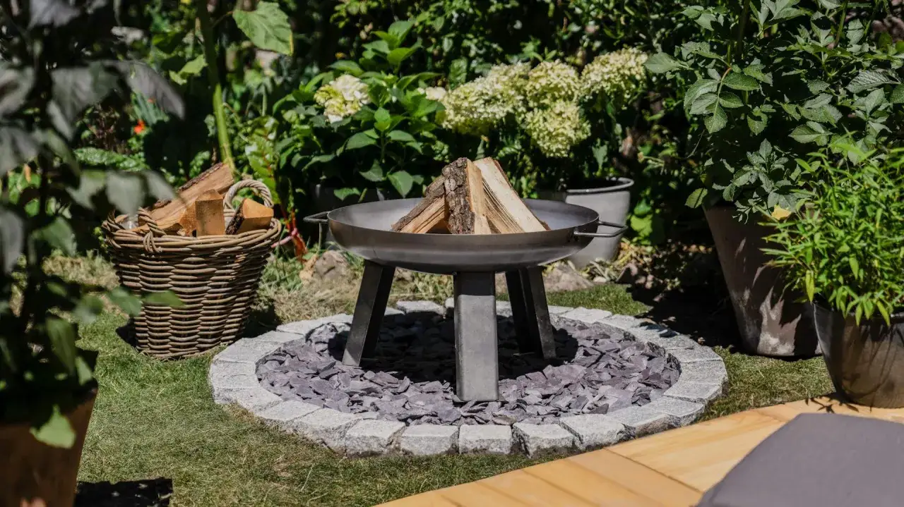 Schöne Feuerstelle im Garten mit Holzkorb und Pflanzen. Tolle Feuerstelle Garten Ideen für gemütliche Abende.