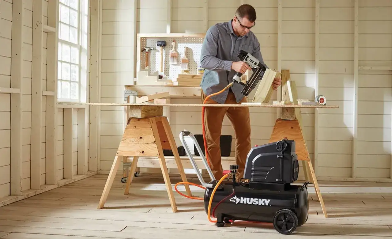 Mann nagelt Holz mit einem Druckluftnagler, der an einem Kompressor 50 Liter angeschlossen ist.