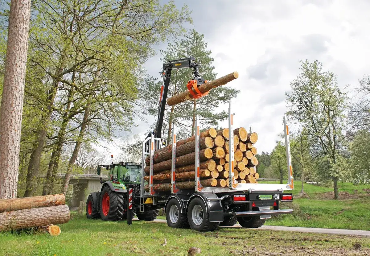 Grüner Traktor lädt mit Kran einen Baumstamm auf einen meterholzwagen voller Holz.