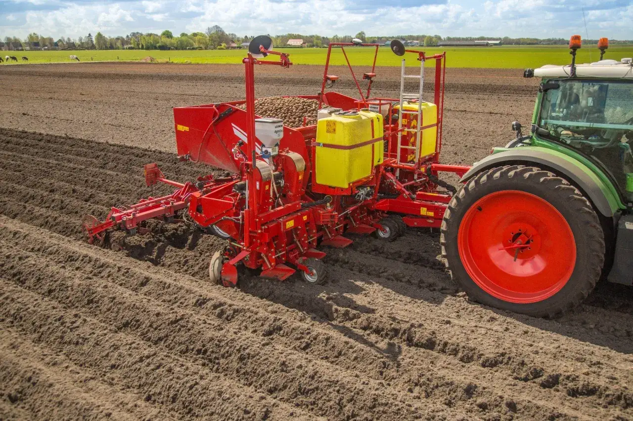 Roter Kartoffelroder mit Granulatstreuer im Einsatz auf einem Feld.