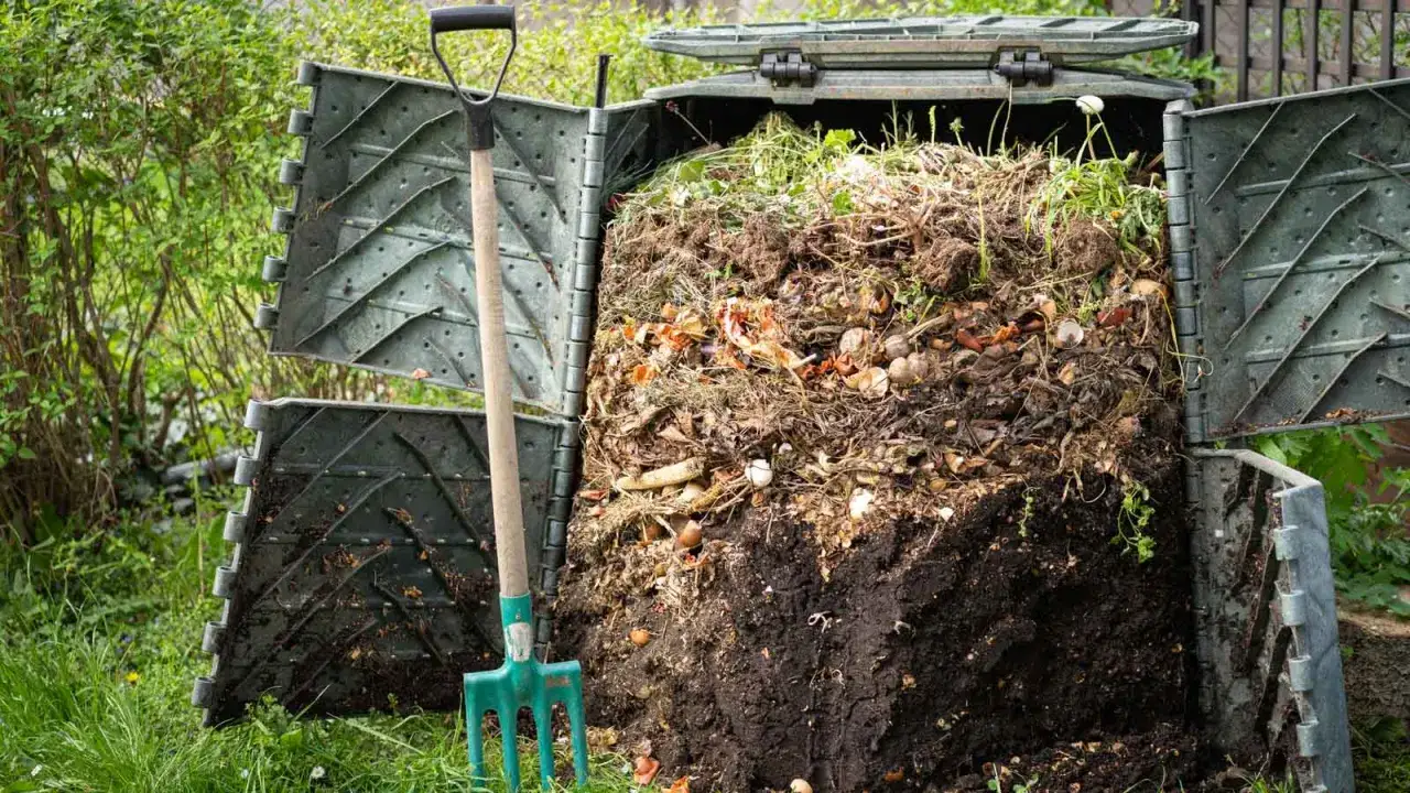 Kompostbehälter mit viel Gartenabfall, bereit zum Eichenlaub kompostieren. Eine Mistgabel steht daneben.