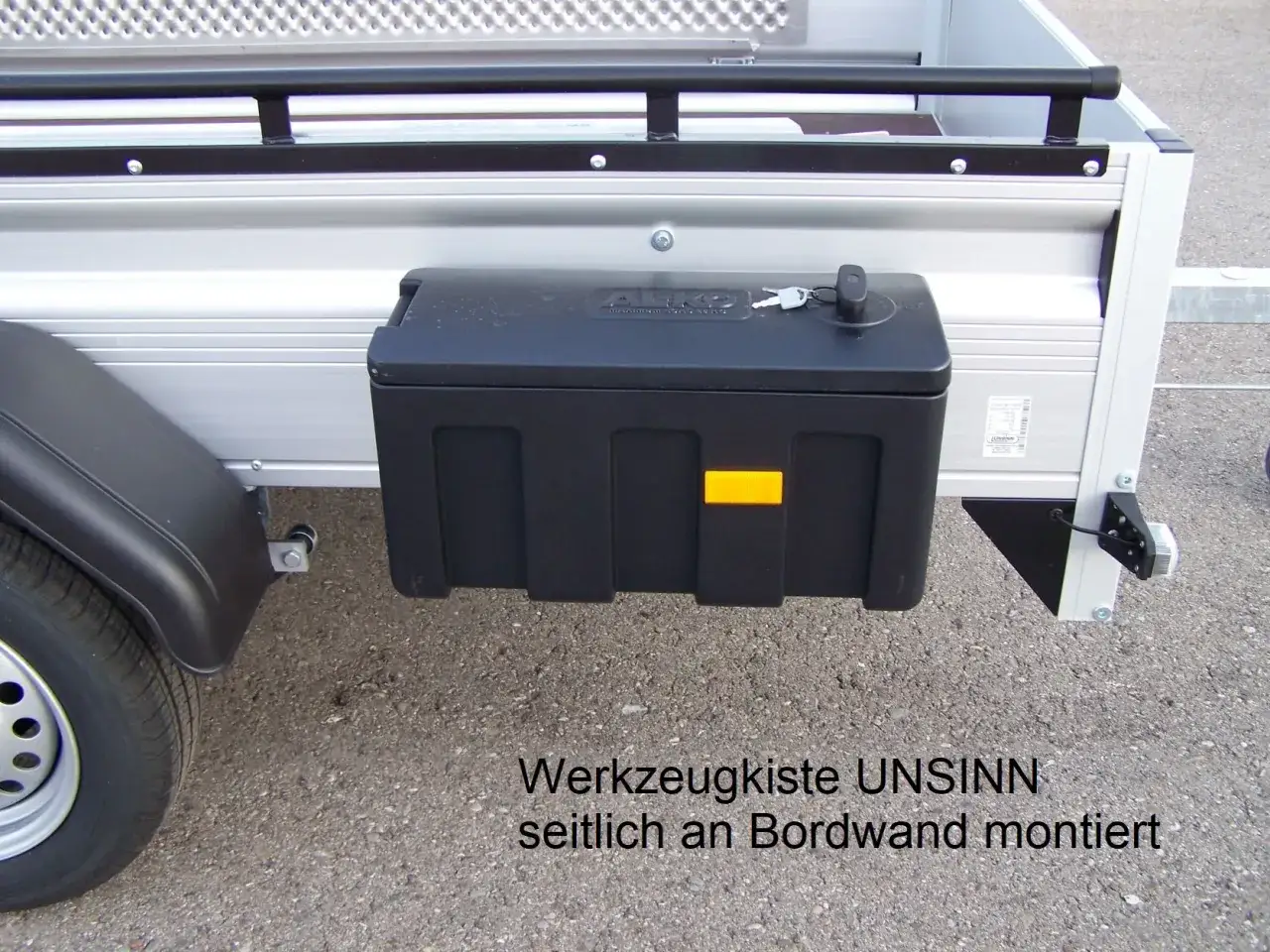 Schwarze Werkzeugbox seitlich am Anhänger montiert, mit Schlüssel.