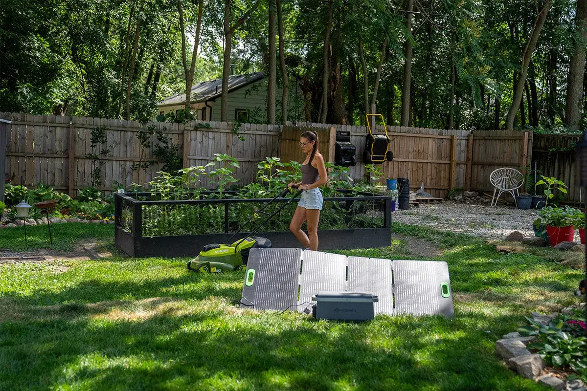 Frau mäht Rasen, während Solarpanels und ein Akku Aggregat im Garten stehen.