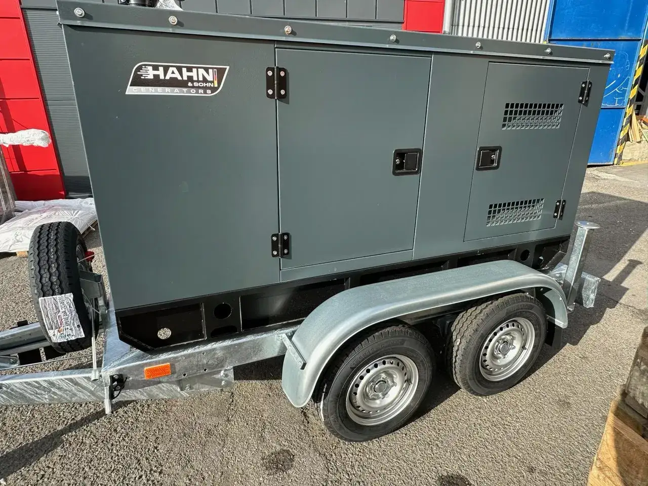 Grauer HAHN & SOHN Generatoren Aggregat Anhänger mit zwei Achsen und Reifen.