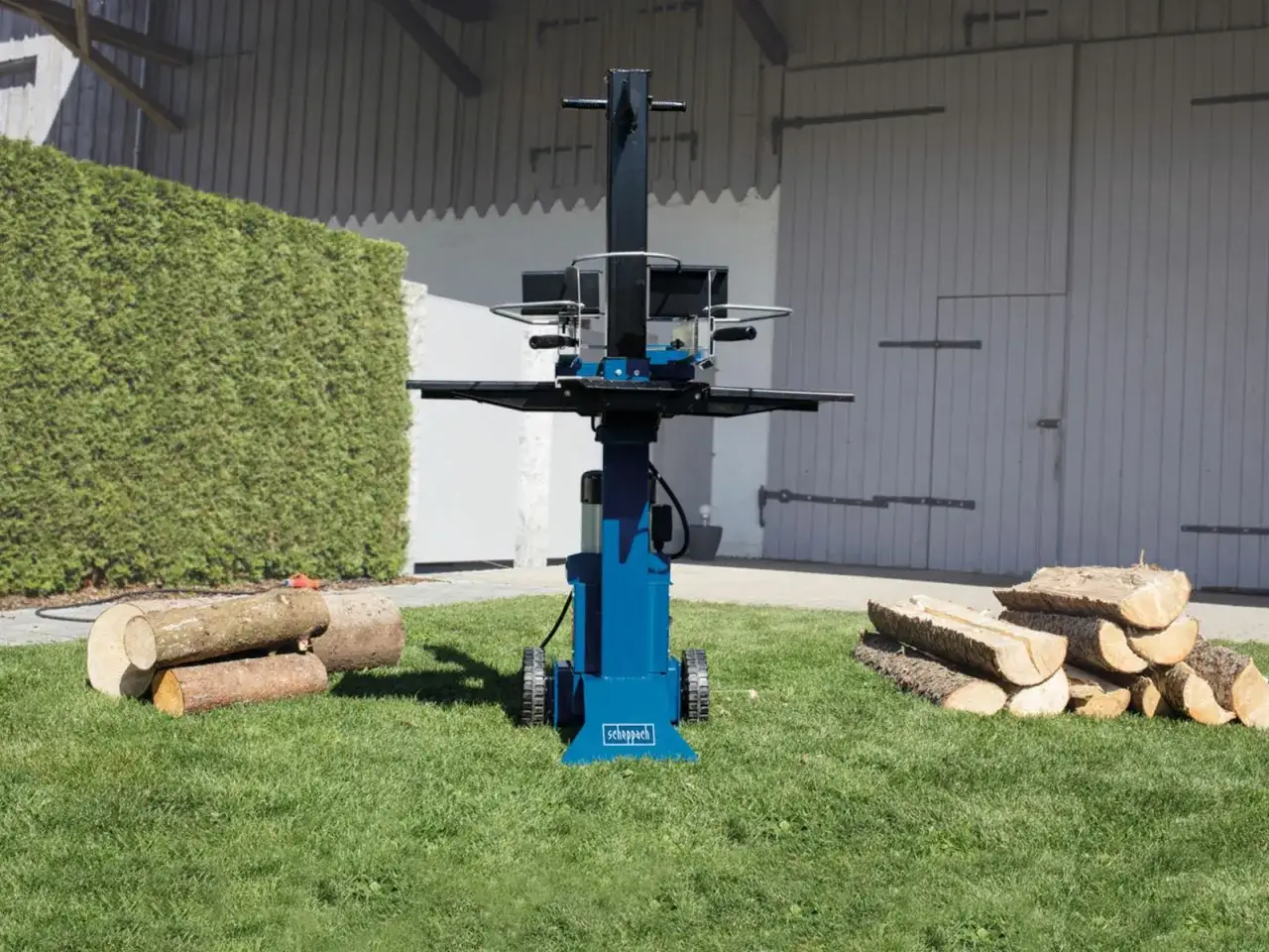 Blauer Holzspalter mit Rädern steht auf grünem Rasen neben Holzstämmen. Ideal für die Zubereitung von Brennholz mit diesem leistungsstarken Holzspalter.