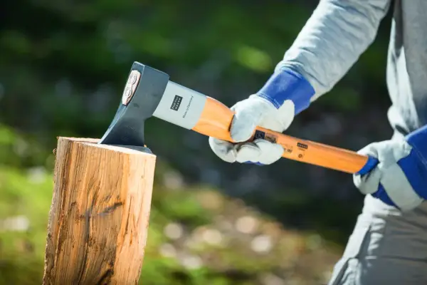 Person mit Handschuhen hält Axt über Holzscheit, bereit, um zu zeigen, wie spaltet man holz.