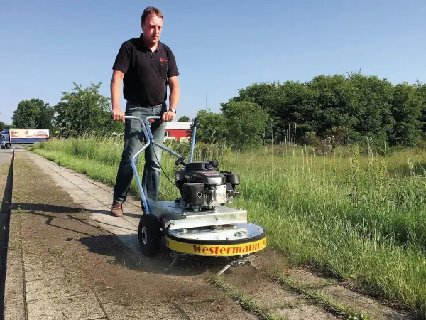Mann mit Westermann Wildkrautbürste auf einem Gehweg, um Unkraut zu entfernen.